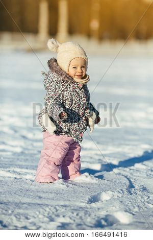 little girl walks through the snow in a warm jaket and hat