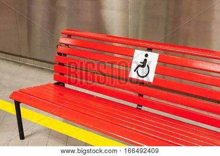 Bench of red color with a sign for disabled people in the public building