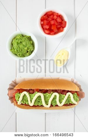 Chilean Completo Italiano (Italian) traditional hot dog sandwich made of bread sausage tomato avocado and mayonnaise ingredients on the side photographed overhead on white wood with natural light (Selective Focus Focus on the hot dog)