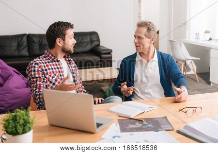 Heated discussion. Nice pleasant handsome men looking at each other and discussing a project while working together in the office