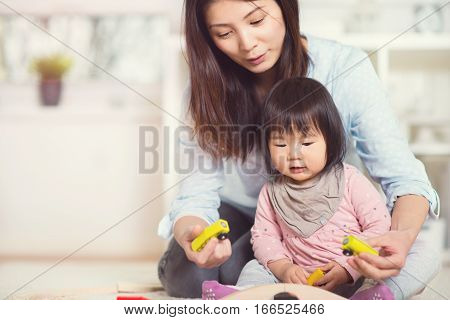 Pretty happy japanese mother play with her cute little toddler daughter at home