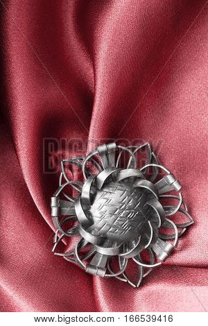 Vintage silver brooch on red draped satin closeup