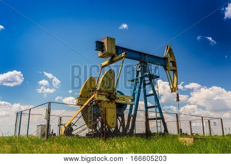 Oil field with pump jack, profiled on blue sky with white clouds, on a sunny day