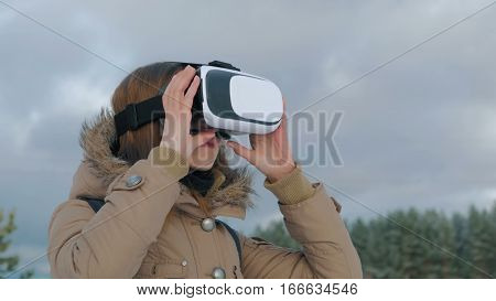 Woman putting on and using virtual reality glasses in winter forest. Virtual reality mask. VR. Future, nature, winter and technology concept