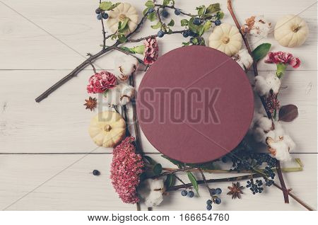 Floristic composition background. Frame made of dried fall flowers, pumpkins, branches and autumn leaves, cotton, sloe and closed round present box. Top view on white wood, flat lay