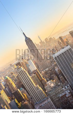 New York City. Manhattan downtown skyline with illuminated Empire State Building and skyscrapers at sunset seen from Top of the Rock observation deck. Vertical composition.