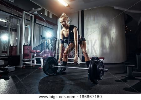 fitness blonde girl prepares for exercising with barbell in gym