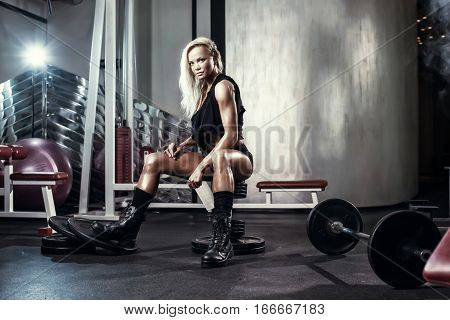 fitness blonde sexy girl posing on bench in the gym in military style clothes