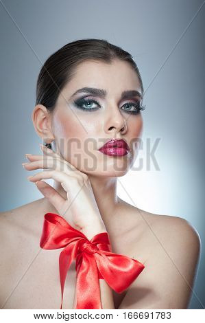 Hairstyle and Make up - beautiful female art portrait with red ribbon. Elegance. Genuine Natural brunette with ribbon - studio shot. Portrait of a attractive woman with beautiful eyes and red lips
