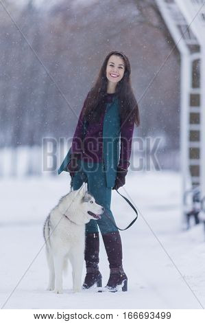 Portrait of Happy Positive Caucasian Brunette Woman Posing With Husky Dog Outdoors. Vertical Image Composition