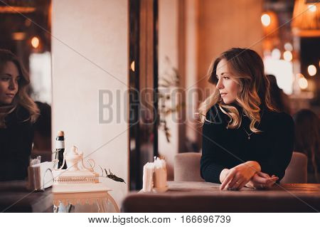 Beautiful blonde girl 20-24 year old sitting in cafe looking at window. 20s. Winter season.