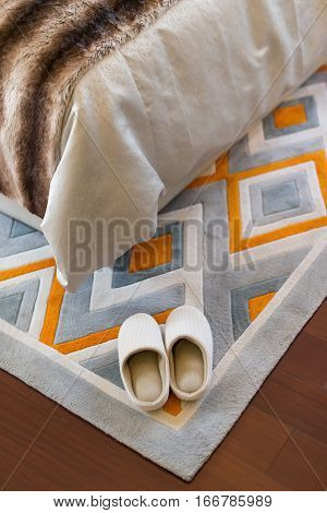 pair of white slippers on carpet nearby a bed