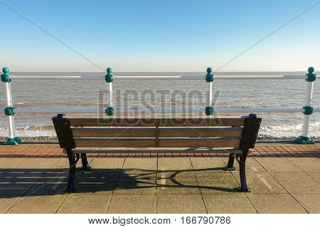 Empty wooden bench on a promenade overlooking the sea on a sunny day in winter.