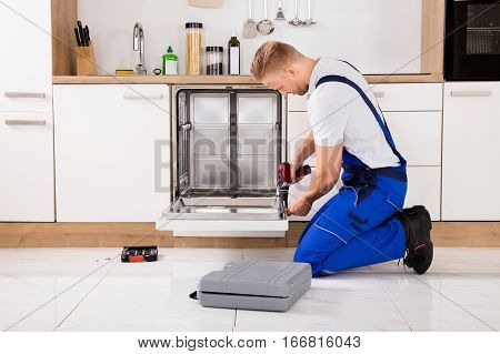 Young Repairman Service Worker Repairing Dishwasher Appliance In Kitchen