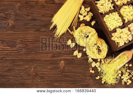 Italian pasta in assortment several different varieties separated in a decorative box on a brown wooden background place for text