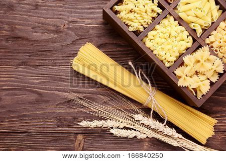 Italian pasta in assortment several different varieties separated in a decorative box spaghetti and ears on a brown wooden background