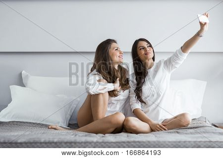 Two Hot Girls Lying  On A Bed Taking A Photo Of Themselves With A Phone