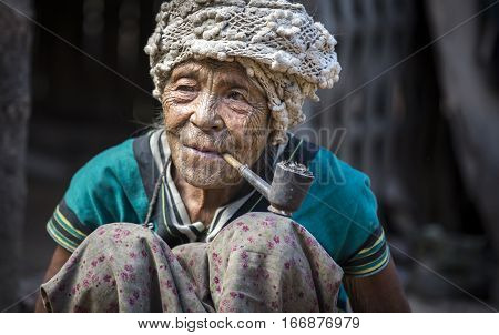 Chin region Myanmar November 11 2014: muun tribe chin lady in her kitchen smoking her pipe