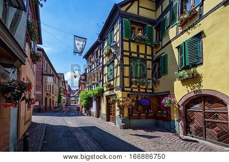 View along the streets of the old French town. Along the street arranged colorful half-timbered houses. In the distance can be seen the figure of tourists.Ribeauville, Alsace.