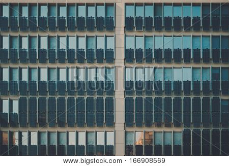 Facade of modern contemporary dark teal office building with a lot of photovoltaic plates on it multiple sun plates on house regular rows of solar batteries in front of windows on daytime