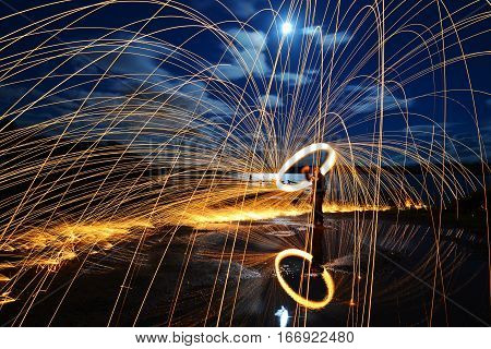 A long exposure of steel wool spinning on a with sparks reflected in a lake