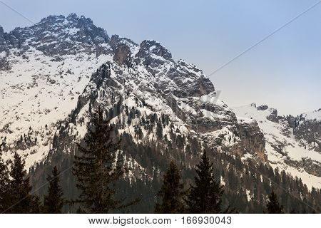Mountain rocky landscape with fir wood forest and snow. Ortisei, Italy. Mountains of South Tyrol in northern Italy. Landscape with sky, fog, snow-capped mountains, forests of fir trees, and snow. Ortisei, Italy