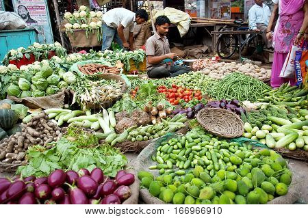 Jaipur India - July 30 2011: Young Indian man at his vegetable shop other vendors in the background. Street vendors provide local people with fresh and cheap produce and are widly spread through out the city