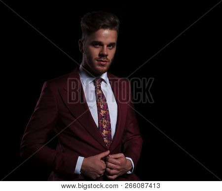 happy young elegant businessman buttoning his coat on black background