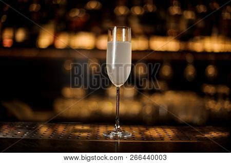 Glass Of A Delicious Cocktail French 75 Standing On The Bar Counter On The Blurred Dark And Yellow L