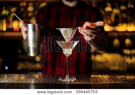 Bartender Holding A Steeel Cocktail Shaker And Sieve Above The Glass On The Steel Bar Counter