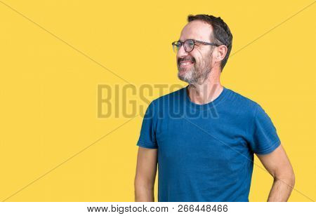 Handsome middle age hoary senior man wearin glasses over isolated background looking away to side with smile on face, natural expression. Laughing confident.