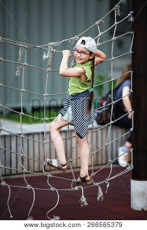 Happy Girl On Outdoor Playground Climbing Frame. Child On Rope Climbing Frame. Selective Focus.