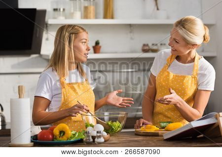 Mature Woman With Adult Daughter Looking At Each Other While Cooking Together