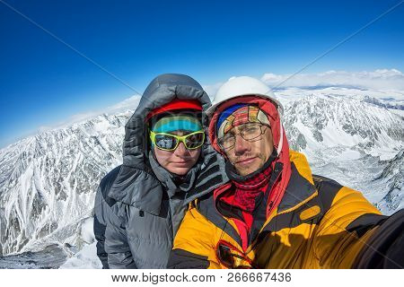 Selfie Couple Climber In Helmet And Down Jacket Stand On Top Of Mountain