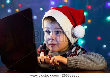 Little Child Writing Letter To Santa Claus On Laptop Computer. Little Boy With Santa Hat.