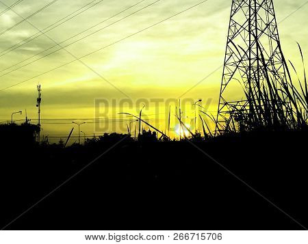 Silhouette Of Electricity Pole With Sunset Background, Contrast Color Of Field Of Grass On Dawn Time
