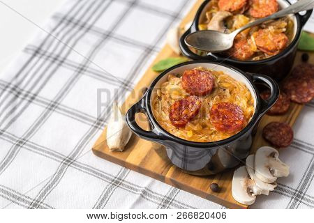 Slovak Christmas National Cabbage Soup In Two Small Black Pots With Sausage On The Tablecloth Backgr