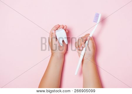 Childs Hands Holding Big Tooth And Toothbrush On Pink Backgroubd. Healty Care Teeth Concept. Top Vie