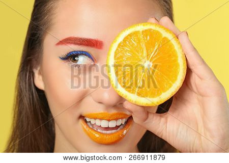 Young woman with dyed eyebrows and half of orange on color background, closeup