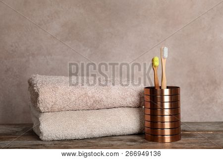 Holder With Bamboo Toothbrushes And Towels On Table Against Grey Background