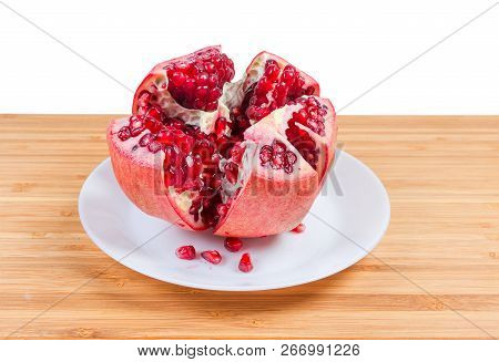 Open Thru Split Ripe Pomegranate Fruit And Several Fallen Out Seeds On The White Dish On A Bamboo Wo