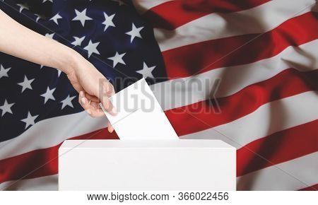 Female Voter Putting Ballot Into Voting Box On Background Us Flag. Concept Of Freedom Democracy With