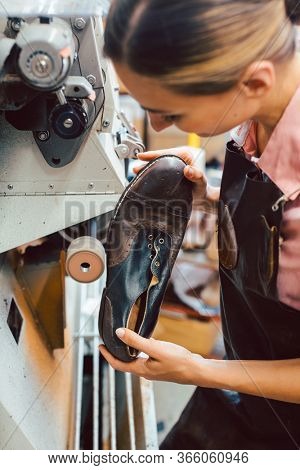 Woman cobbler working on machine in her shoemaker workshop adjusting the settings