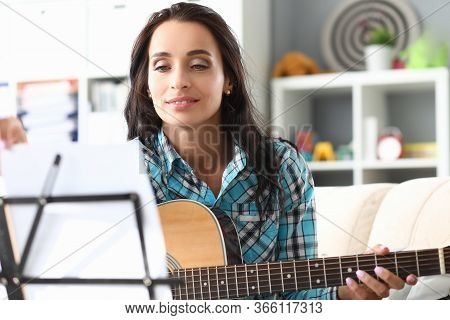 Portrait Of Woman Playing Guitar And Looking Carefully At Notes. Smiling Brunette Learning New Tune.