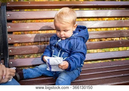 Baby Hygiene Outside And Hand Wash Idea Concept. Little Cute Baby In Blue Clothes Sits On A Bench In