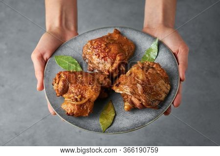 Filipino Chicken Adobo On Gray Plate In Female Hands. Chicken Adobo Is Filipino Cuisine Dish Of Brai