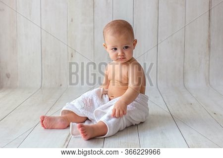 One Yeat Old Baby Girl Is Sitting On Wooden Backgroun In White Towel. After Bath Time.
