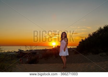 Woman In A White Dress On A Background Of The Sea At Sunset.