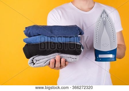 Ironing Clothes Concept. Cropped Photo Of A Man Holding Stack Of Folded Clothes And An Iron Isolated