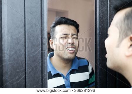 An Indian Male In Casual T-shirt Giving Wierd Expression At His Reflection In Mirror